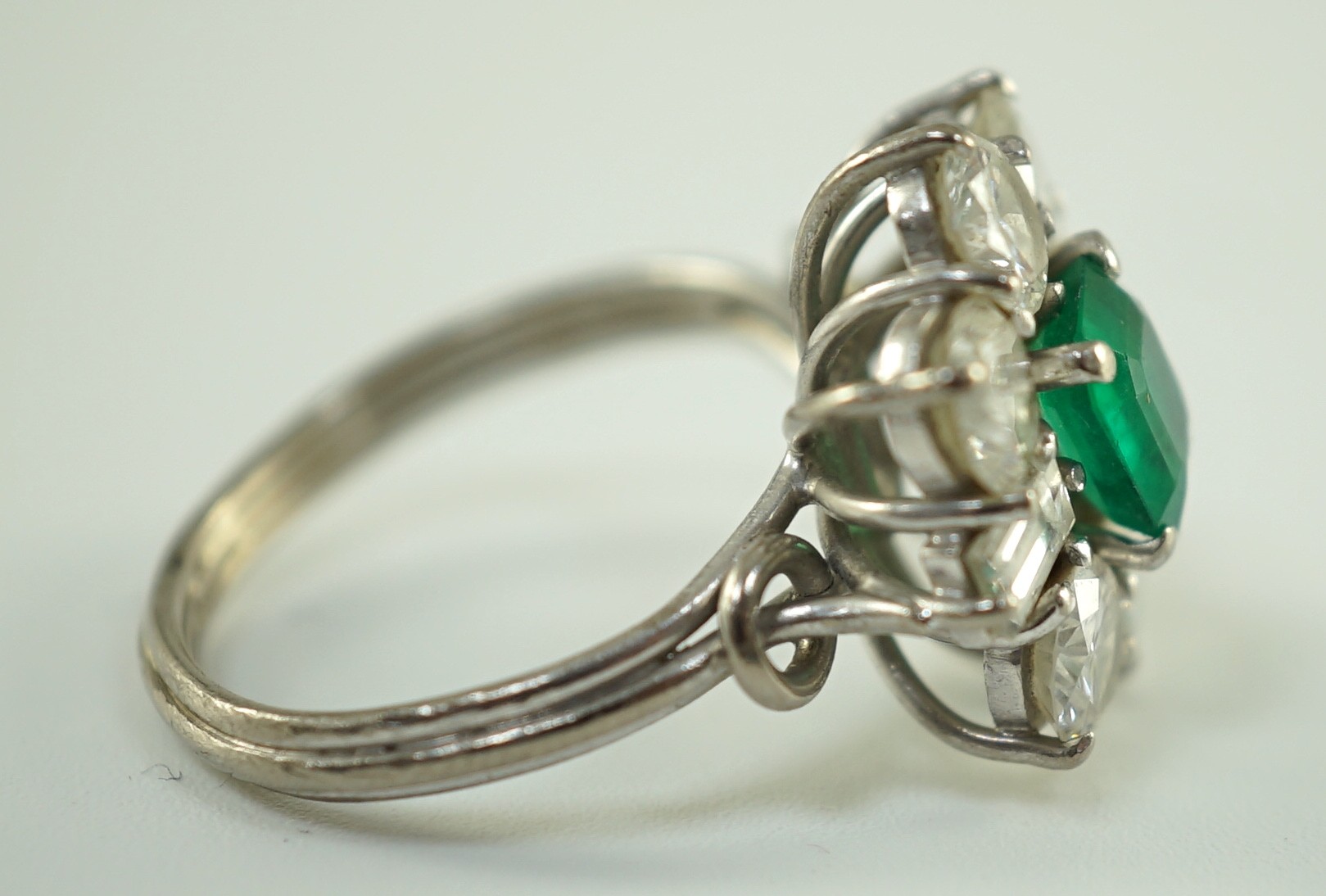 A mid 20th century 18kt white gold, single stone emerald and round and baguette cut diamond cluster ring